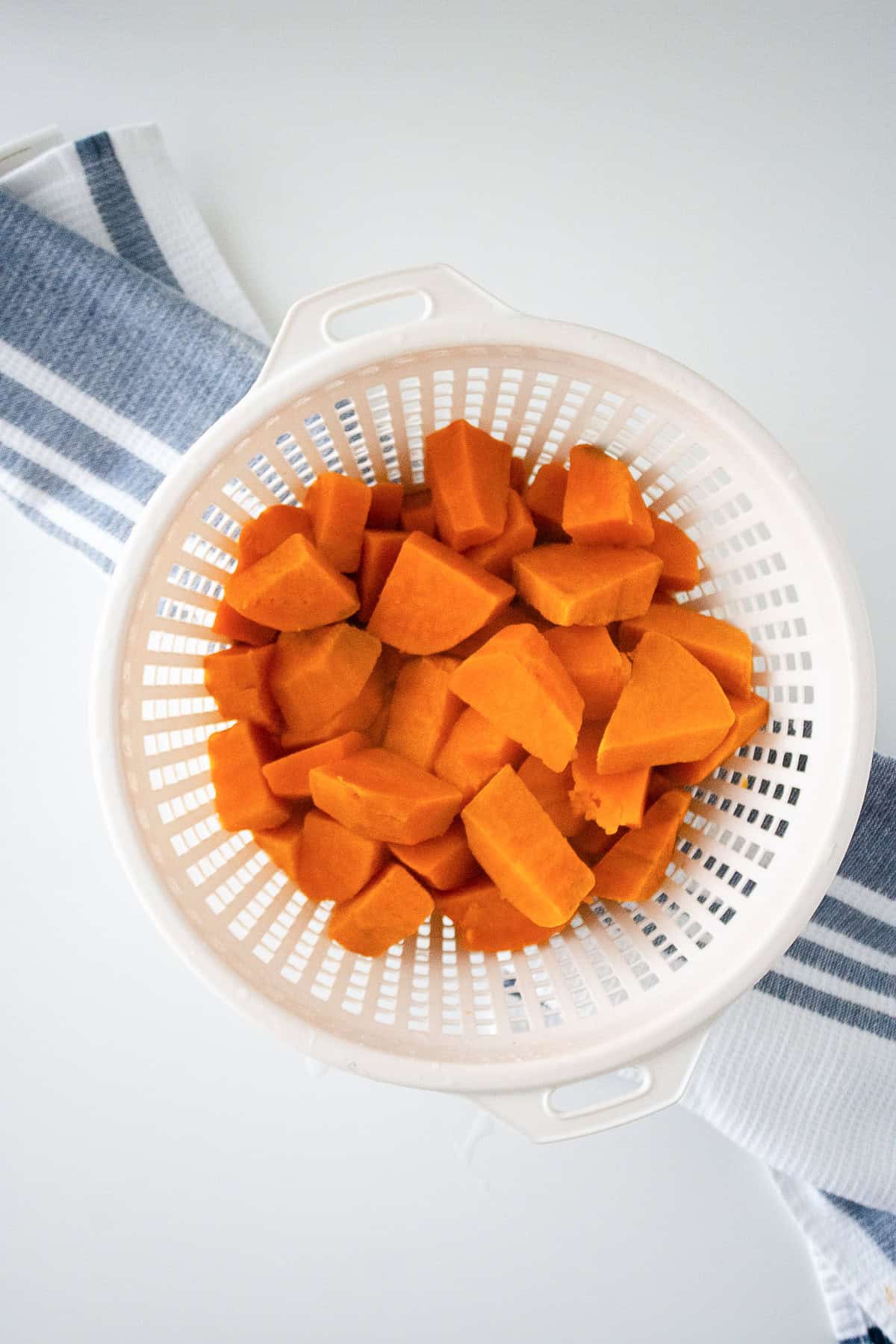 Cooked sweet potato chunks drained in a white colander after boiling.