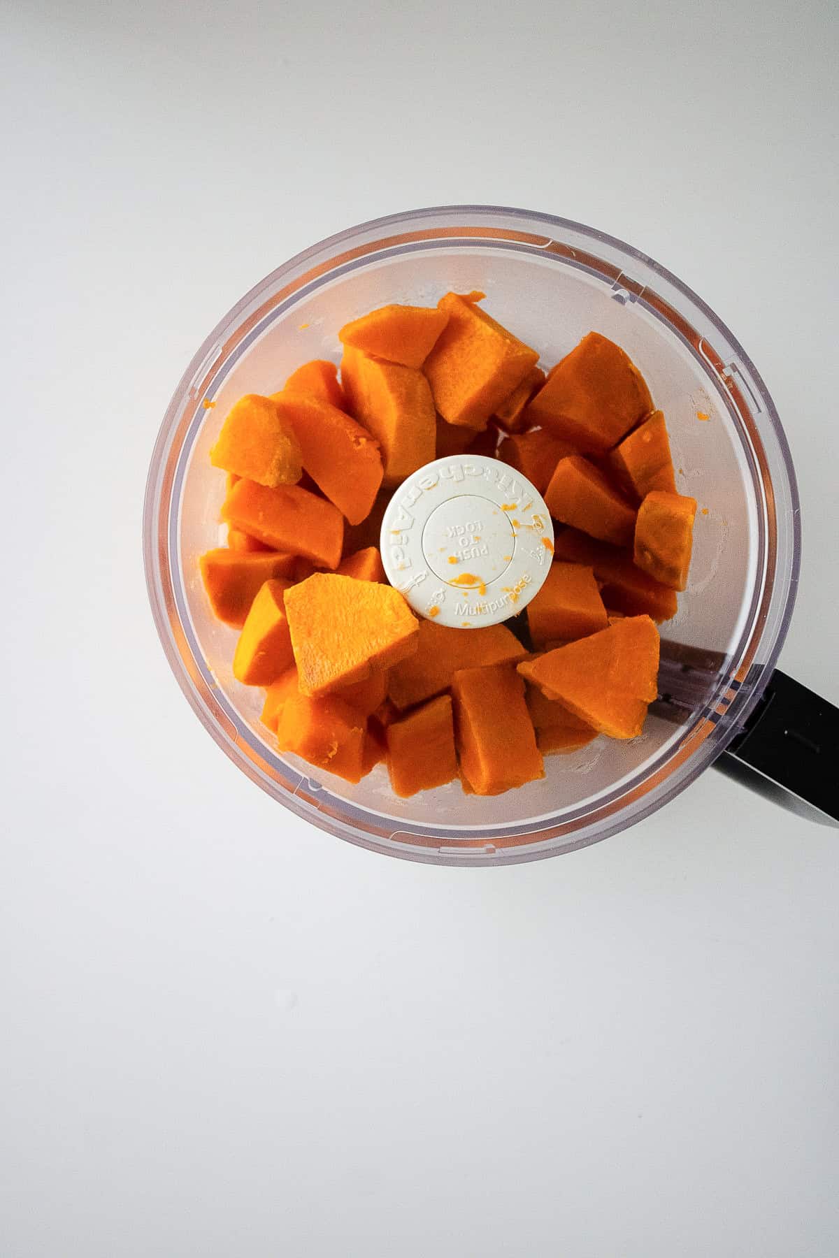 Sweet potatoes are blended into a smooth puree inside a food processor bowl.