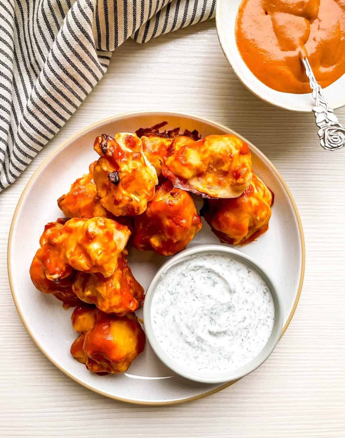 Plate of vegan buffalo cauliflower wings served with creamy dairy-free ranch dipping sauce.
