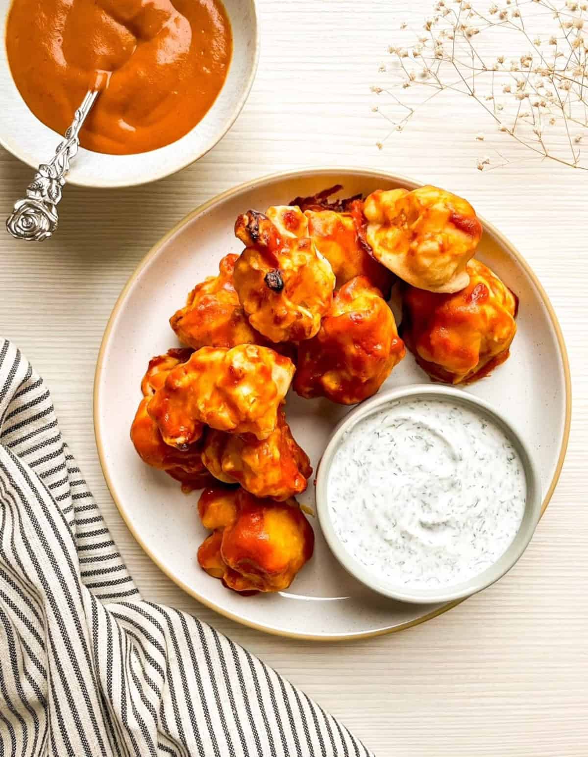 Overhead view of vegan buffalo cauliflower wings with ranch dip and buffalo sauce on a light tabletop.
