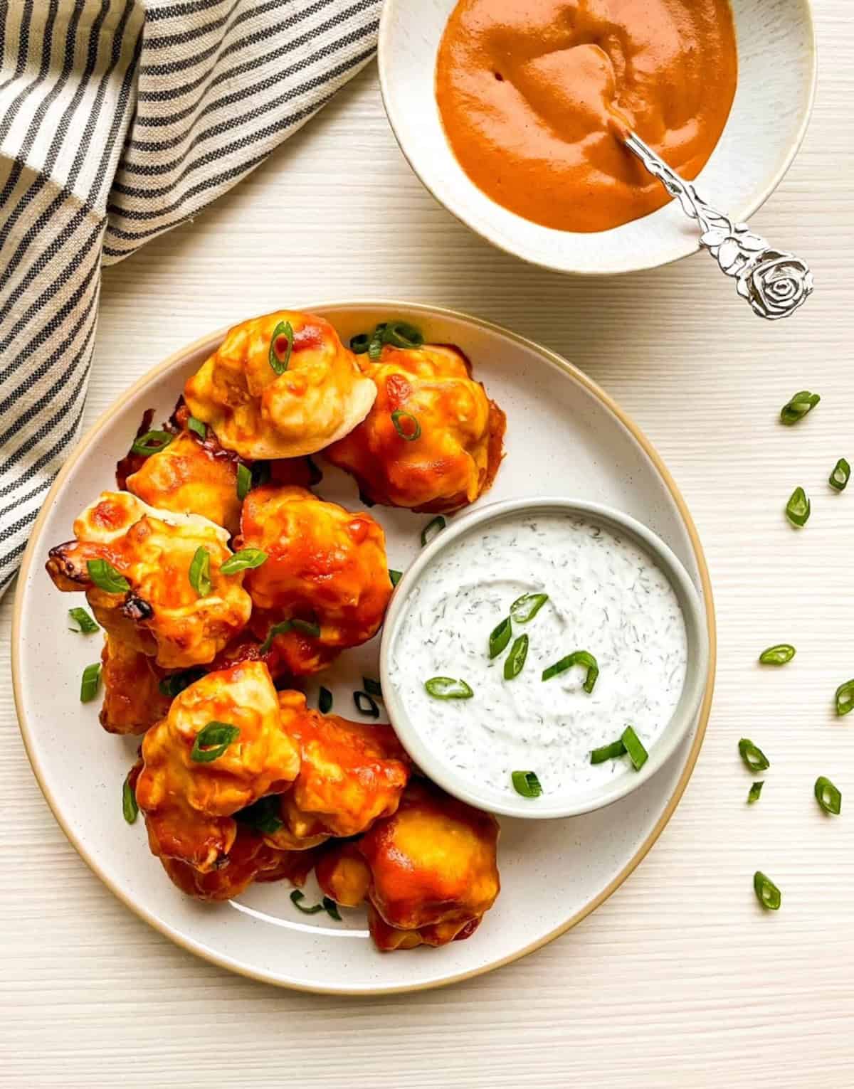 Overhead view of vegan buffalo cauliflower wings topped with green onions and served with ranch dressing.