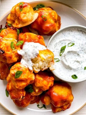 Close-up of vegan buffalo cauliflower wings with a cauliflower piece dipped in dairy-free ranch dressing showing the interior texture.