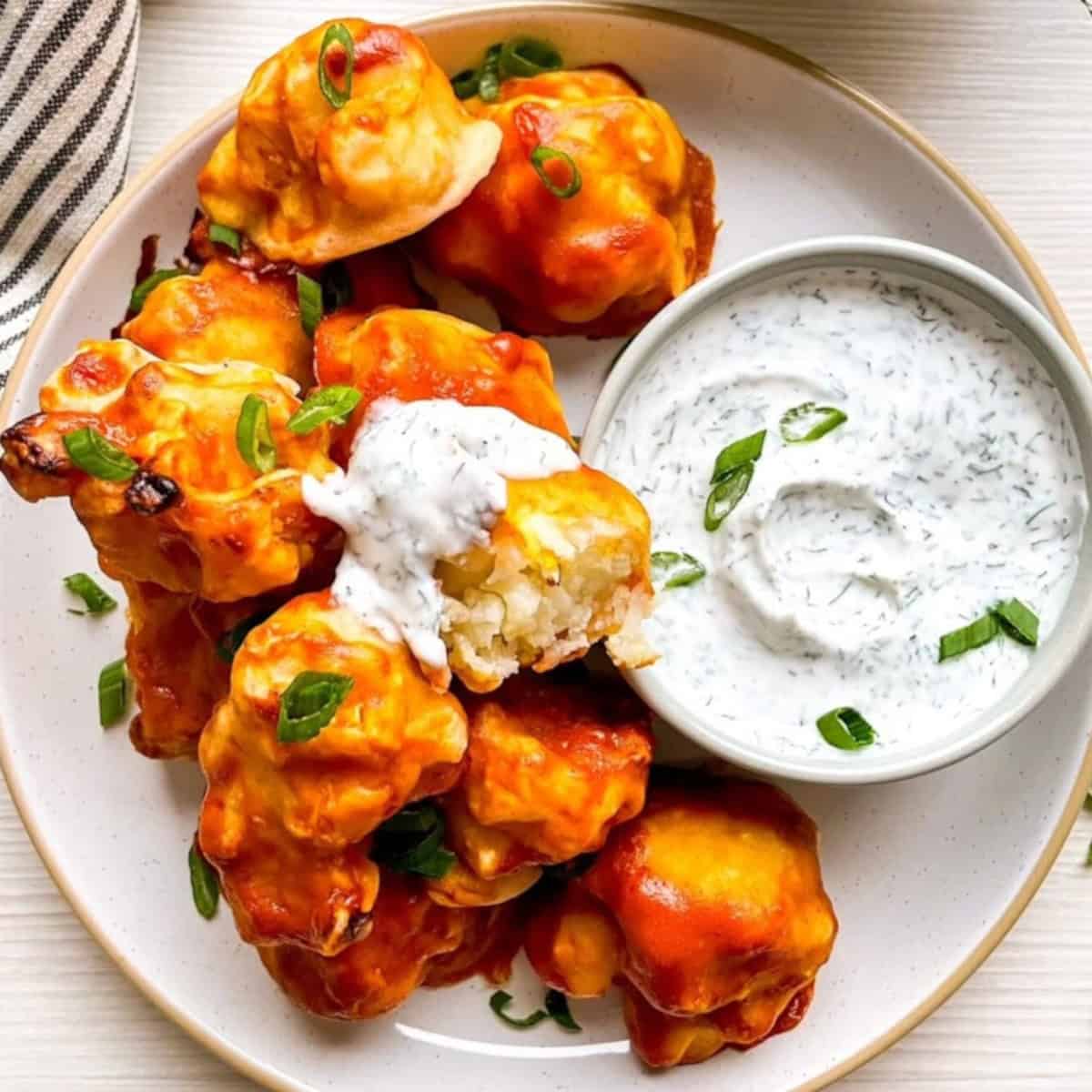 Close-up of vegan buffalo cauliflower wings with a cauliflower piece dipped in dairy-free ranch dressing showing the interior texture.