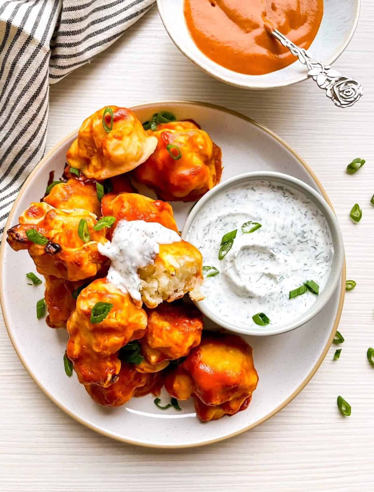Close-up of vegan buffalo cauliflower wings with a cauliflower piece dipped in dairy-free ranch dressing.