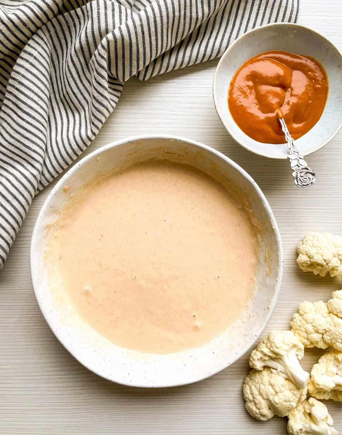 Buffalo cauliflower batter mixed until smooth in a large bowl with cauliflower florets on the side.