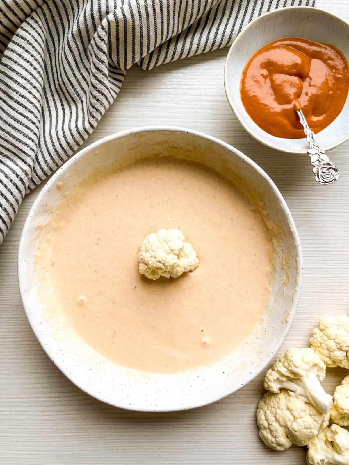 Cauliflower floret dipped into seasoned batter before baking for vegan buffalo cauliflower wings.