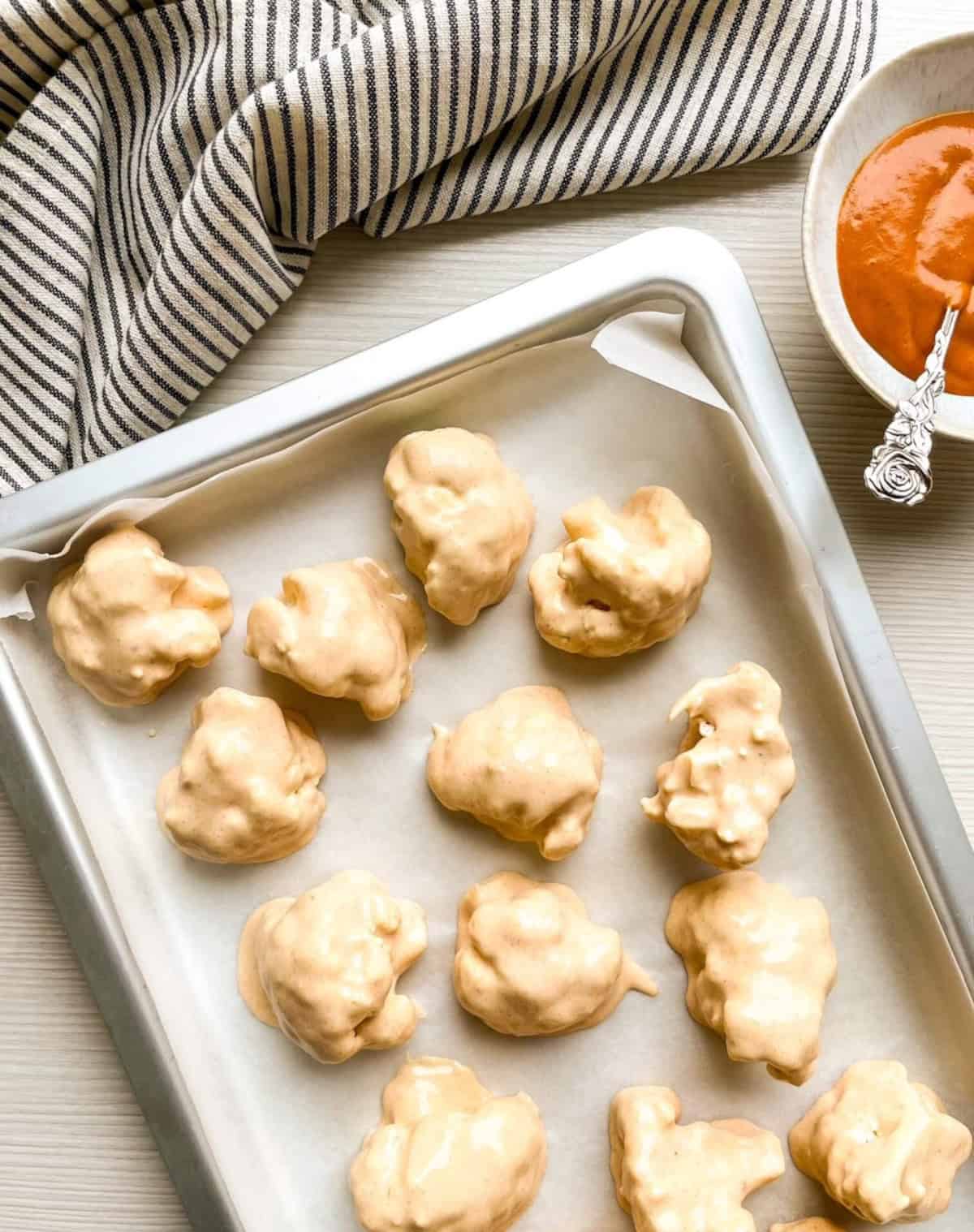Batter-coated cauliflower florets arranged on a parchment-lined baking sheet before baking.