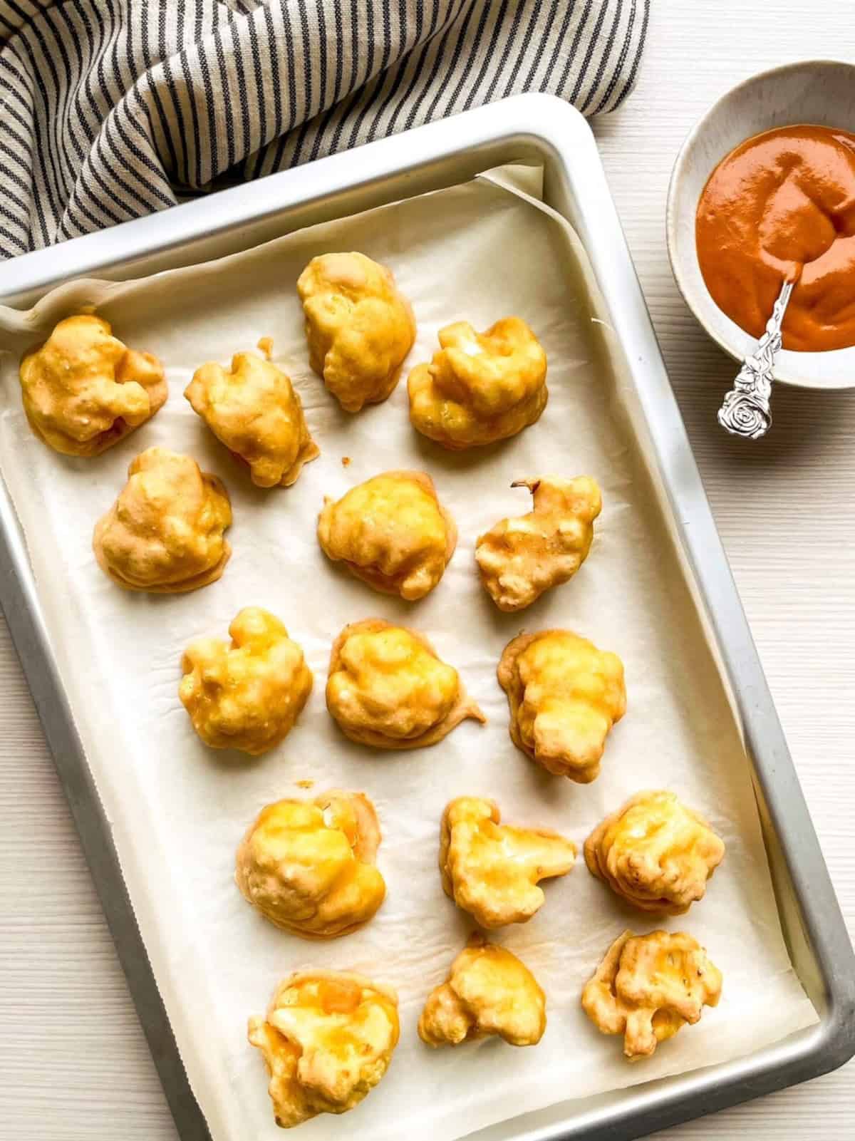 Baked cauliflower florets on a baking sheet after the first bake before adding buffalo sauce.
