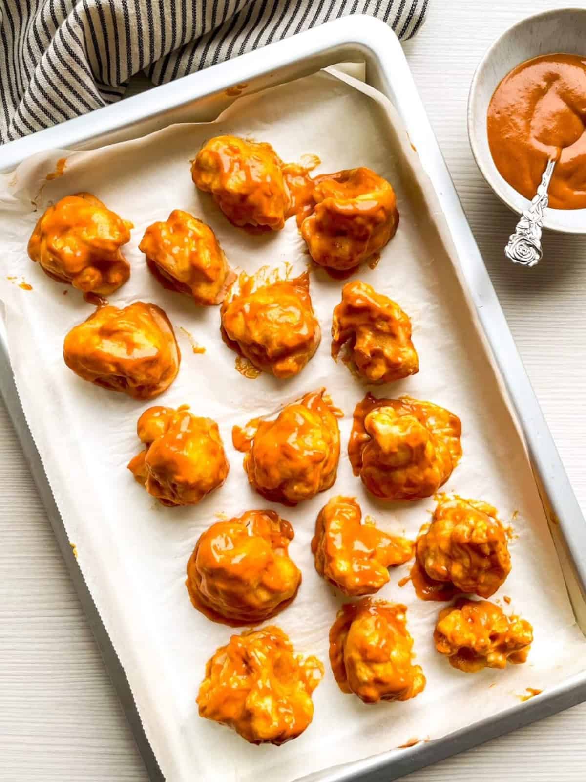Baked cauliflower florets coated with buffalo sauce on a parchment-lined baking sheet.