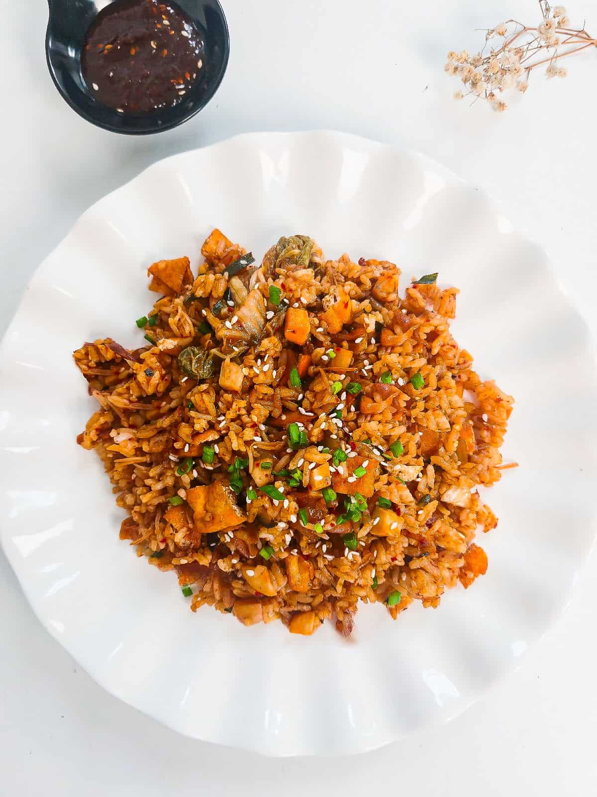 Overhead view of vegan kimchi fried rice with tofu, mushrooms, and sesame seeds served on a white plate.
