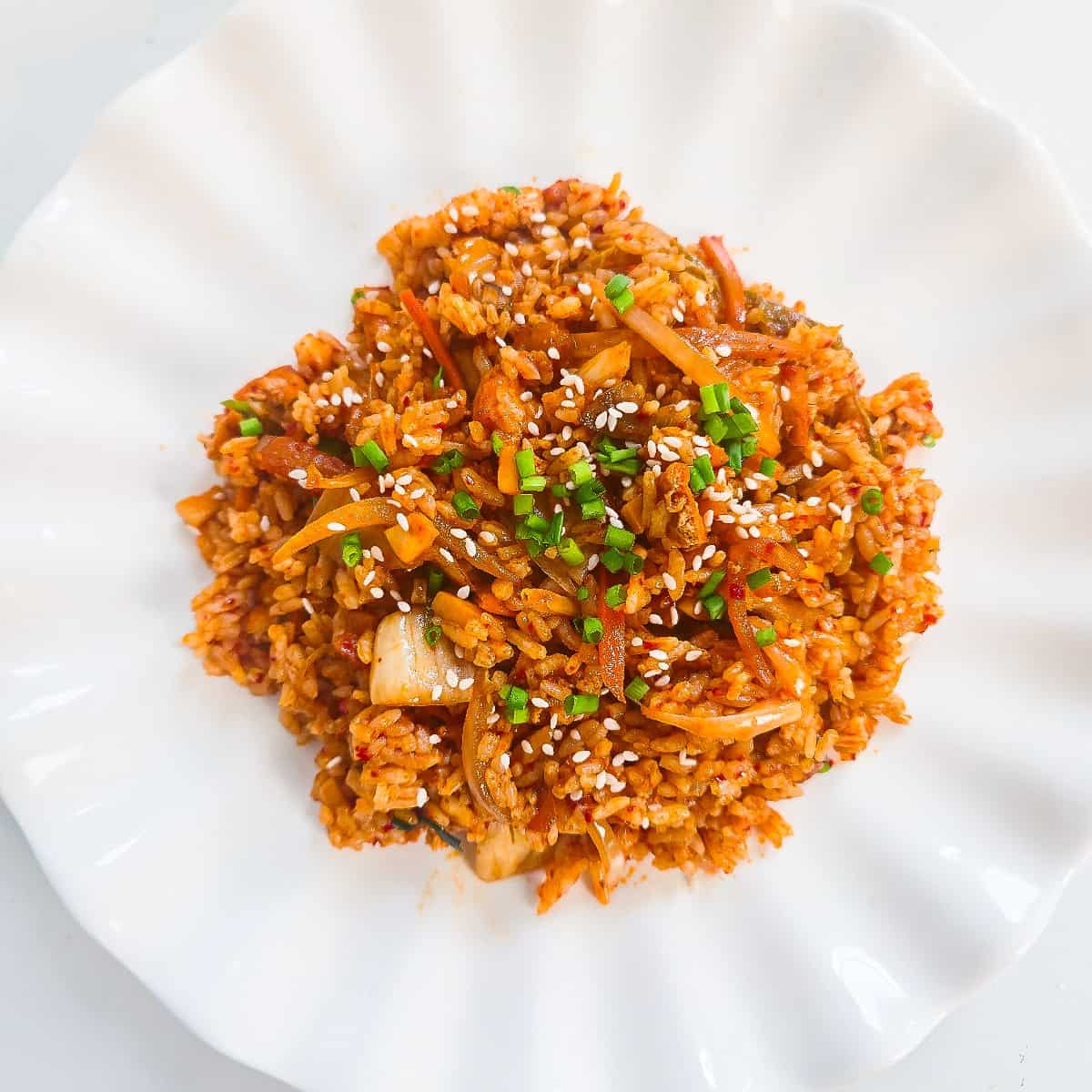 Close-up of vegan kimchi fried rice topped with green onions and sesame seeds on a white plate.