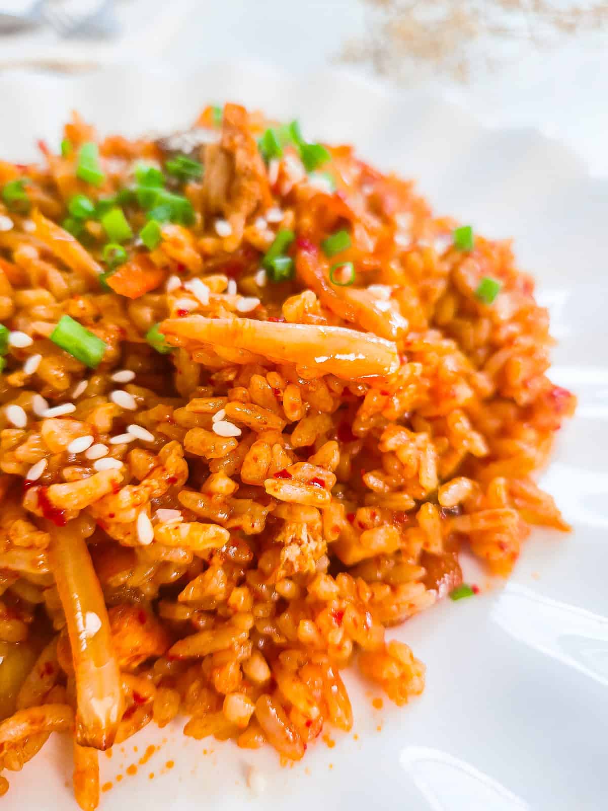 Forkful of vegan kimchi fried rice with tofu, kimchi, and mushrooms lifted above a white plate.