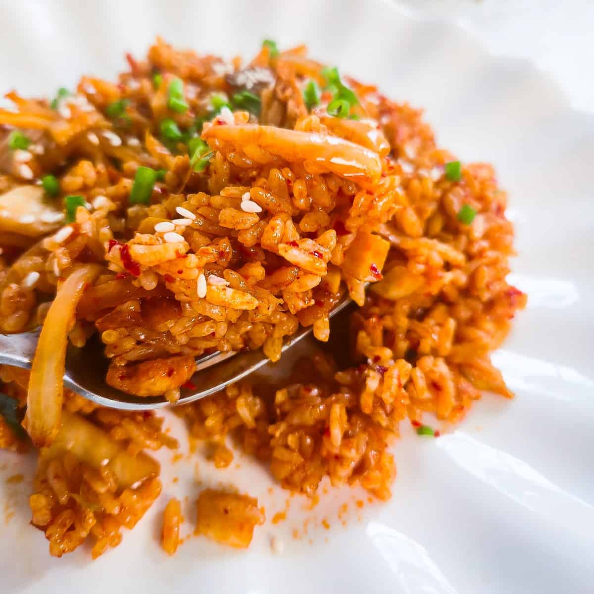 Vegan kimchi fried rice served on a white plate and garnished with sesame seeds and green onions.