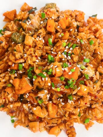 Close-up overhead view of vegan kimchi fried rice topped with sesame seeds and chopped green onions on a white plate.