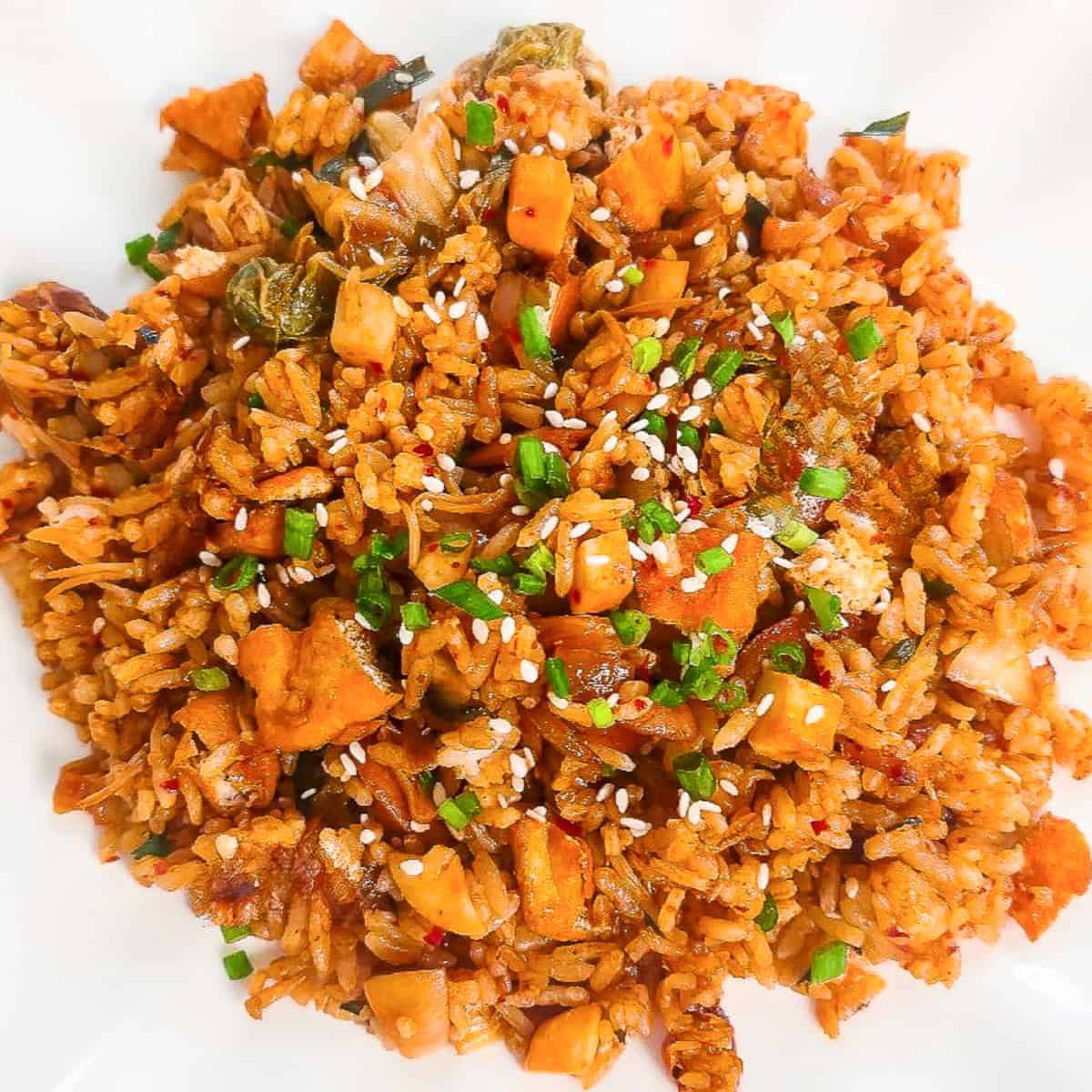 Close-up overhead view of vegan kimchi fried rice topped with sesame seeds and chopped green onions on a white plate.