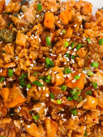 Vegan kimchi fried rice with tofu, kimchi, sesame seeds, and green onions served on a white plate.