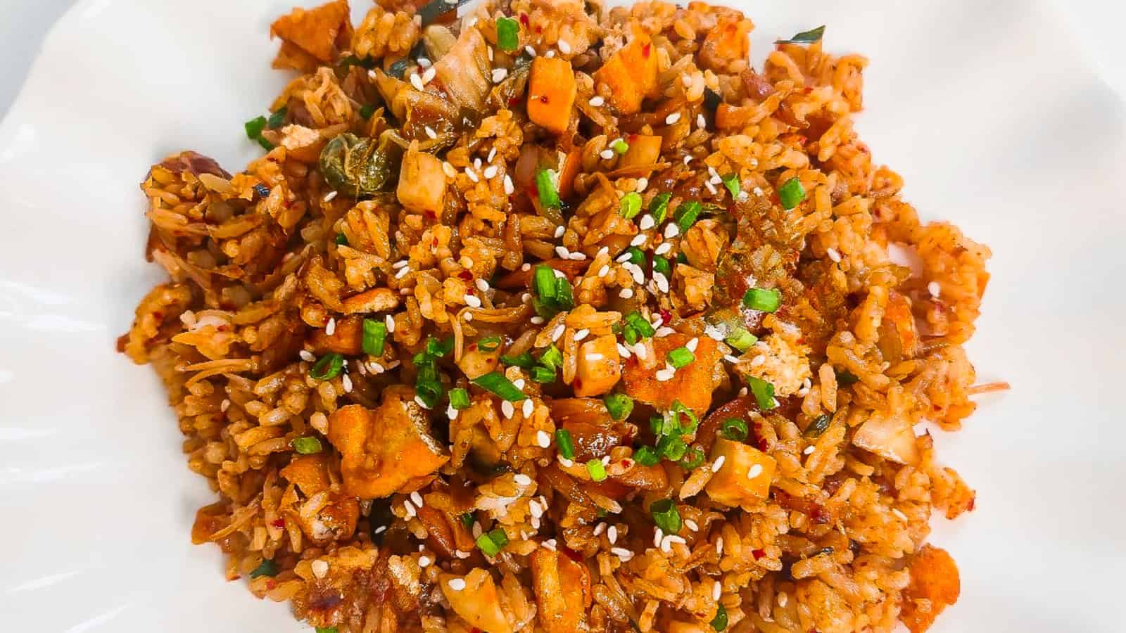 Vegan kimchi fried rice with tofu, kimchi, sesame seeds, and green onions served on a white plate.