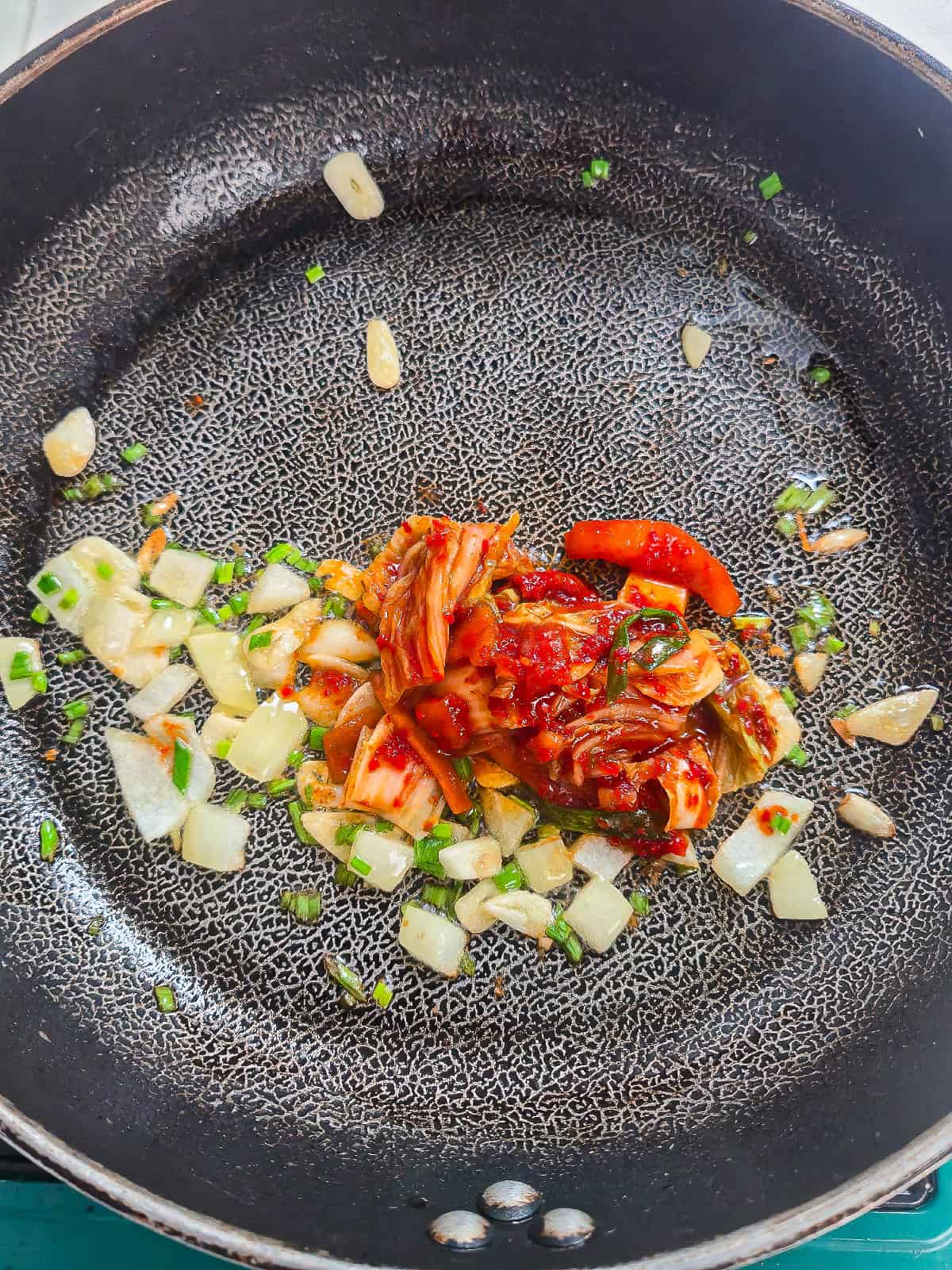 Garlic, diced onion, and green onions saut&eacute;ing in a skillet for vegan kimchi fried rice.
