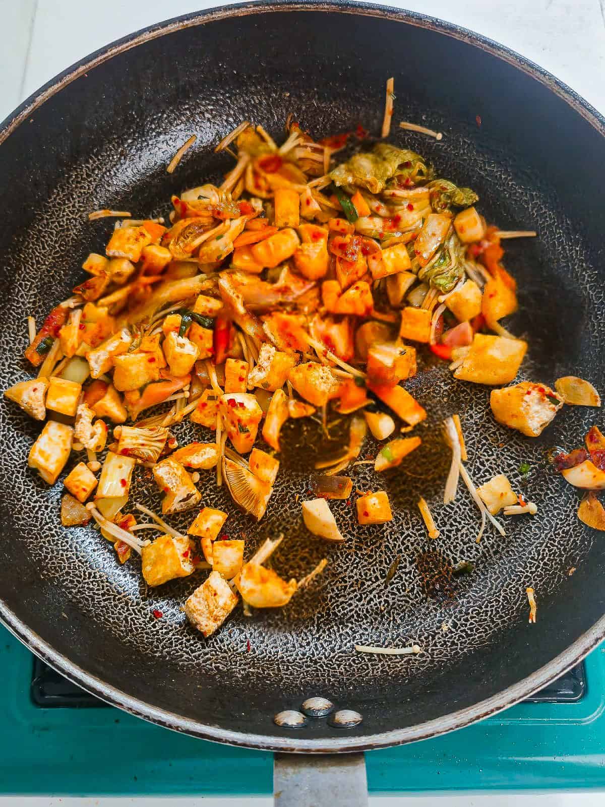 Fried tofu puffs, mushrooms, and kimchi cooking together in a skillet.