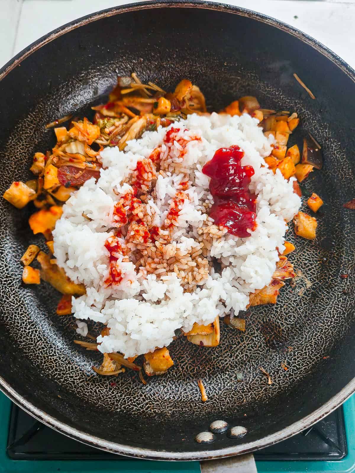 Cooked rice, soy sauce, and gochujang added to tofu, mushrooms, and kimchi in a skillet.