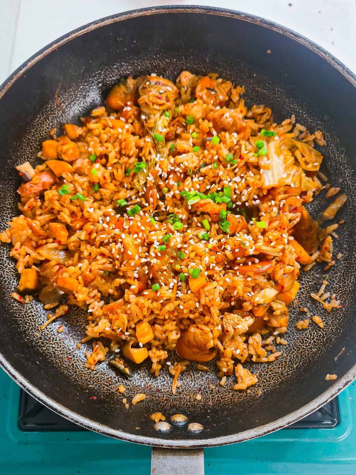 Vegan kimchi fried rice is stirred together in a skillet and topped with sesame seeds and green onions.