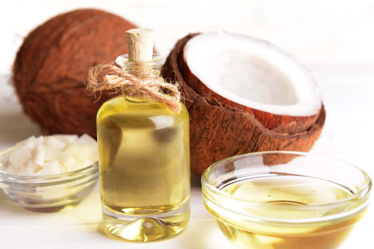 Coconut oil in glass containers with fresh coconut halves and coconut flakes on a white surface.