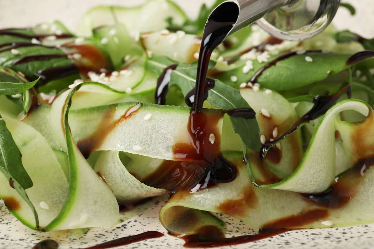 Balsamic glaze drizzled over cucumber ribbons with greens and sesame seeds.