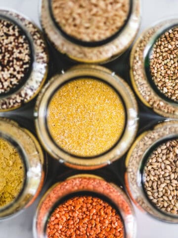 Assorted vegan pantry staples including grains, lentils, quinoa, and nutritional yeast in jars.