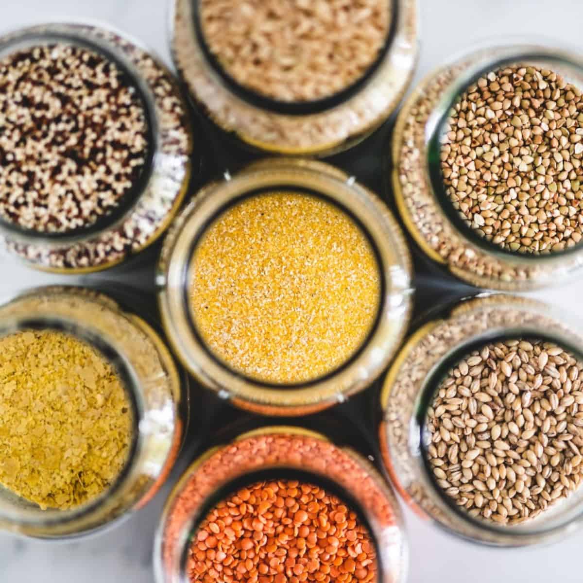 Assorted vegan pantry staples including grains, lentils, quinoa, and nutritional yeast in jars.