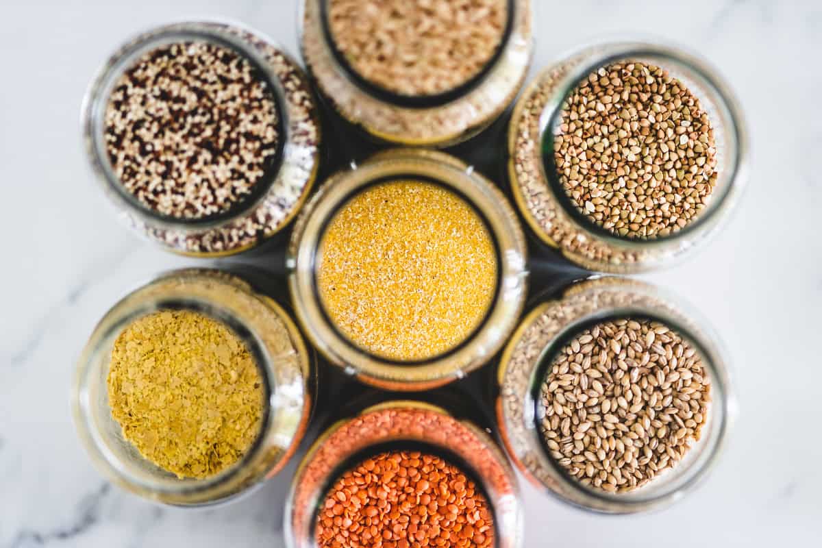Assorted vegan pantry staples including grains, lentils, quinoa, and nutritional yeast in glass jars.