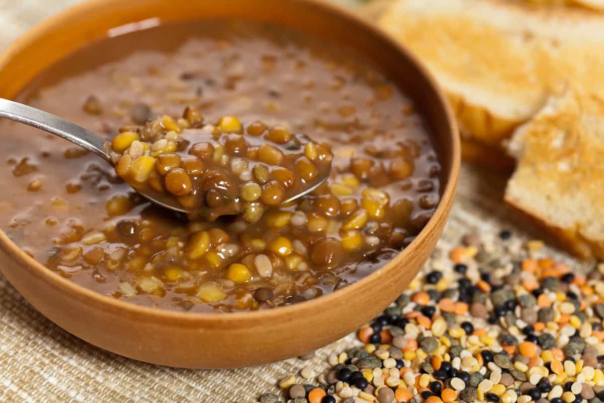 Hearty lentil soup in a bowl with mixed lentils and a spoon, served with slices of crusty bread.