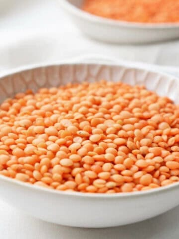 Dry red lentils in a white bowl on a light cloth background, ready for microwave cooking.