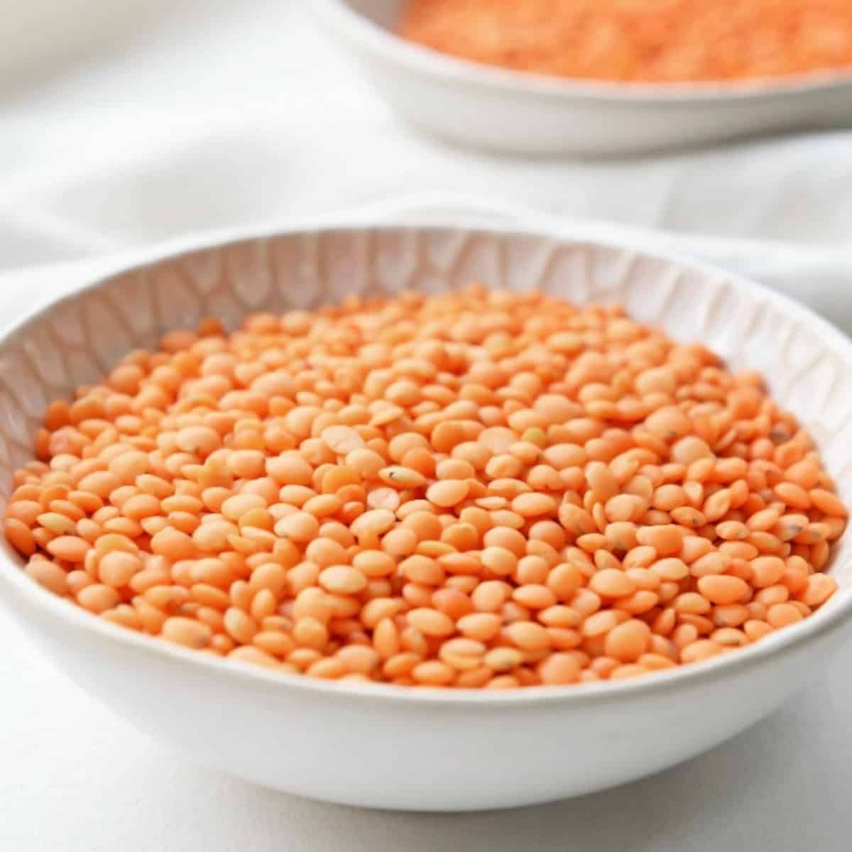 Dry red lentils in a white bowl on a light cloth background, ready for microwave cooking.