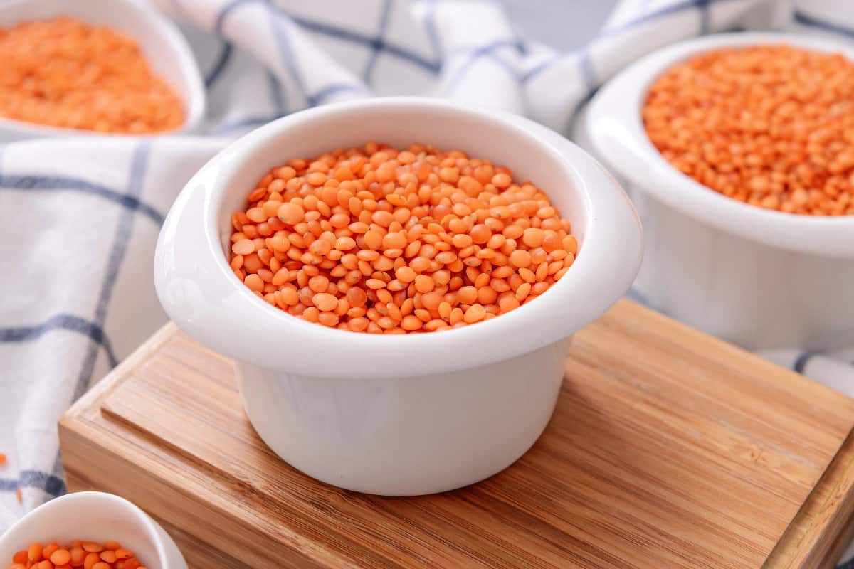 Red lentils in a white ramekin on a wooden board, an easy ingredient for microwave recipes.