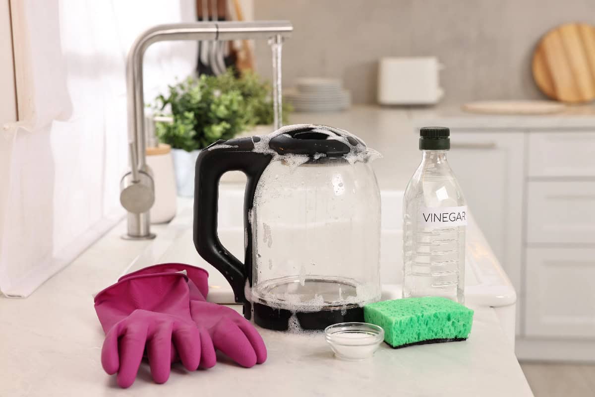 Electric kettle with cleaning supplies, including vinegar, sponge, and rubber gloves, ready for descaling.