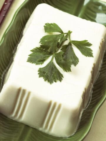 Silken tofu block on a leaf-shaped plate with chopsticks, a popular plant-based egg substitute.