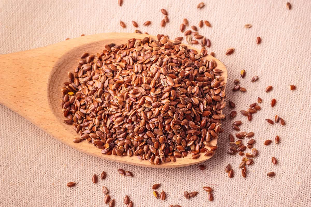 Brown flaxseeds in a wooden spoon, commonly used to make a flax egg for vegan baking.