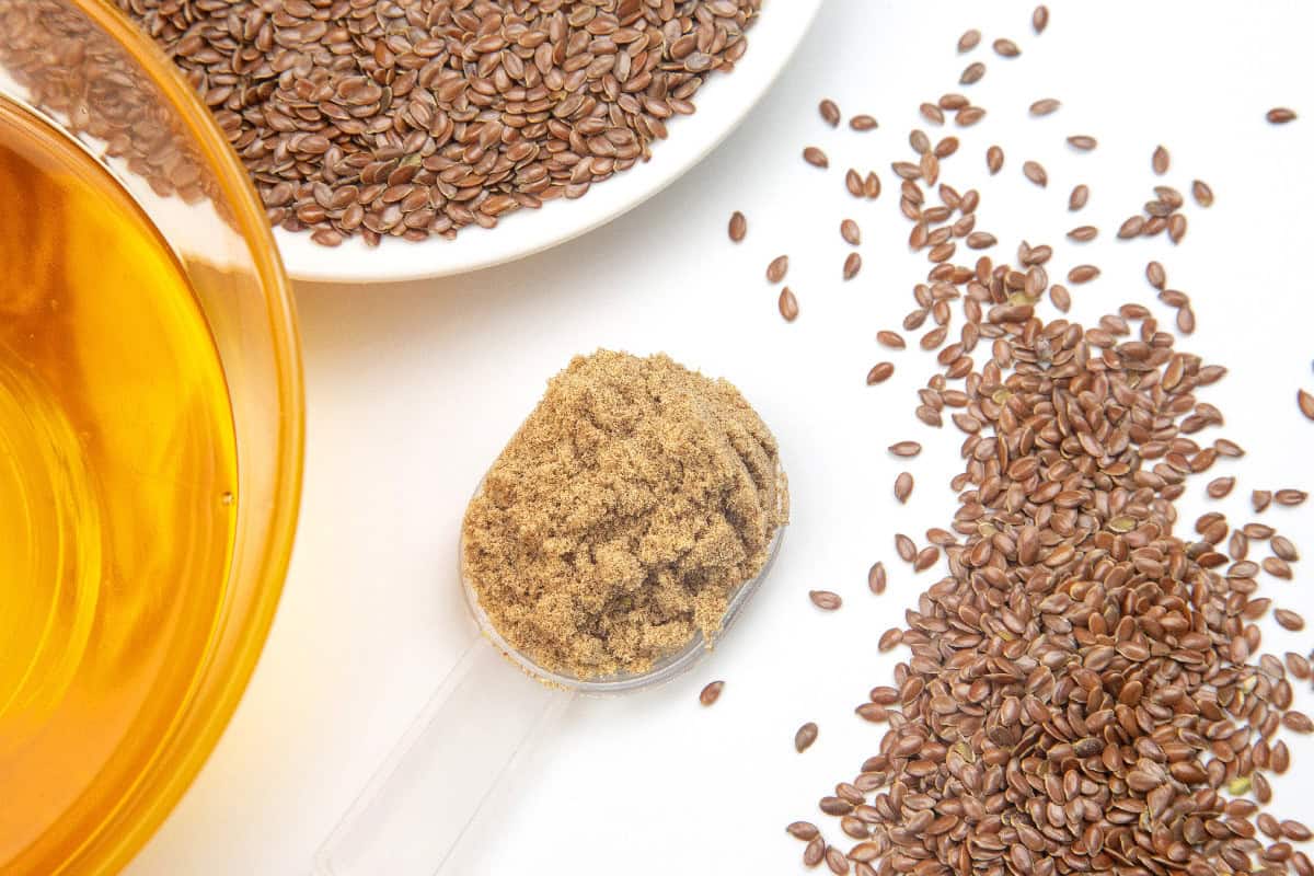 Ground flaxseed beside whole flaxseeds and oil, ingredients used to make a flax egg substitute.