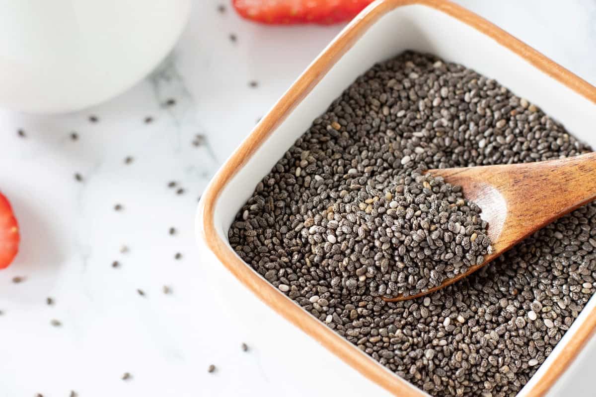 Chia seeds in a ceramic bowl with a wooden spoon, a nutritious vegan egg replacement for baking.