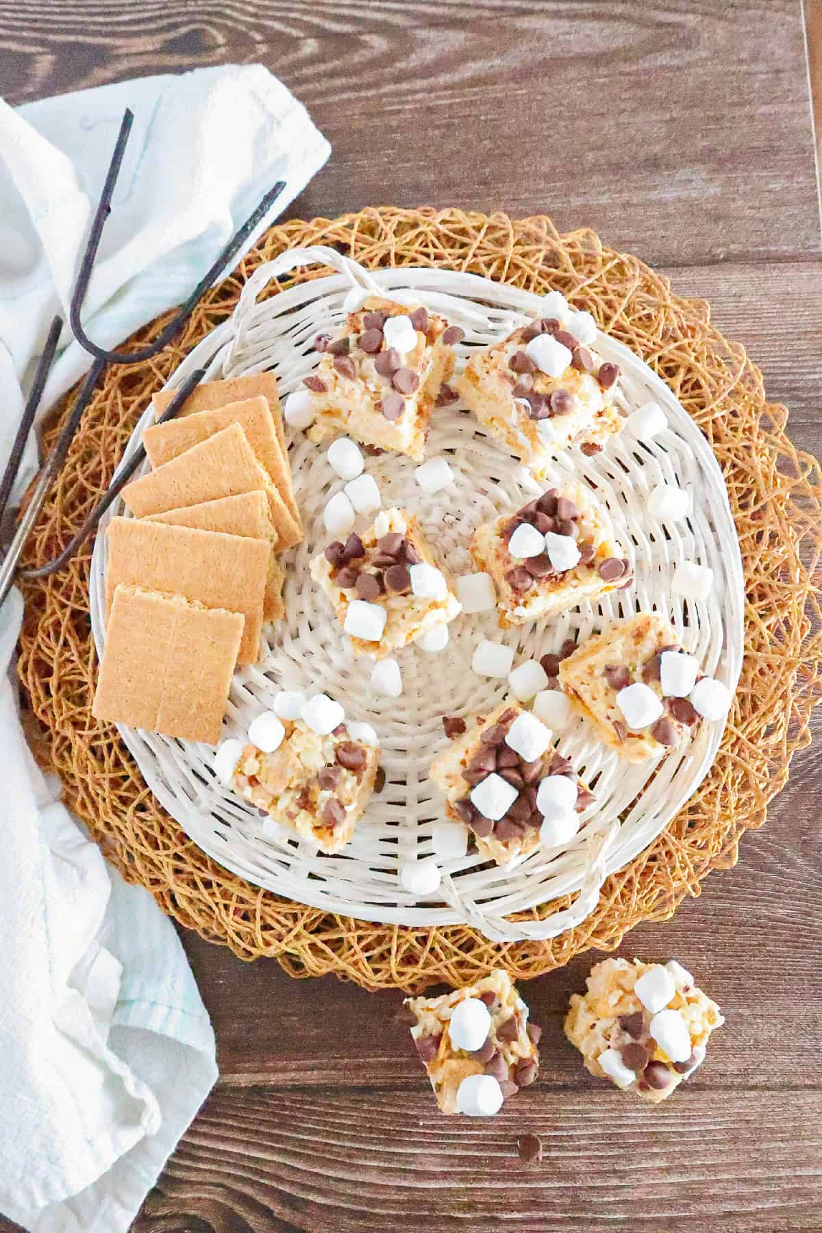 Overhead view of homemade S'mores Rice Krispie treats arranged in a white basket with graham crackers and mini marshmallows.