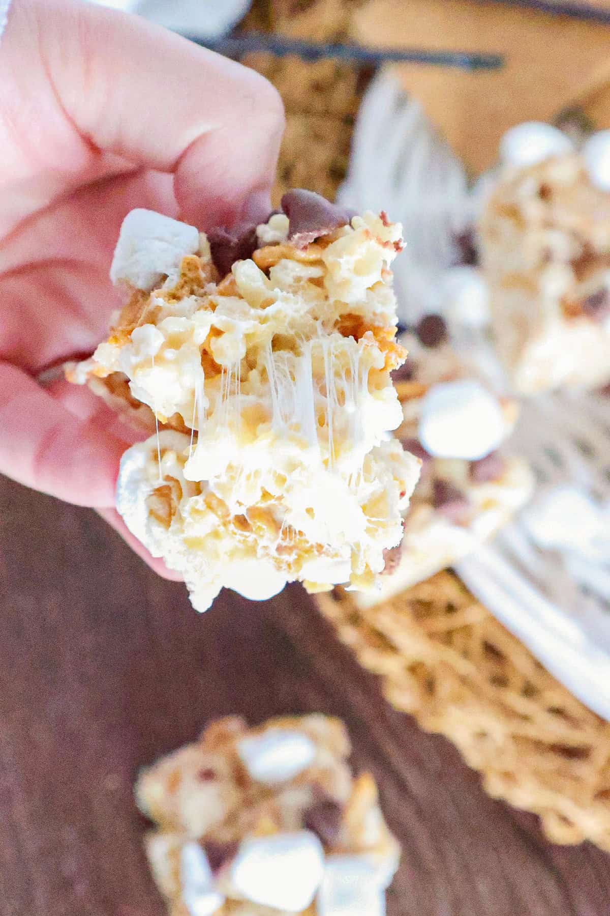 Hand pulling apart a gooey S'mores Rice Krispie treat with melted marshmallow and chocolate chips.