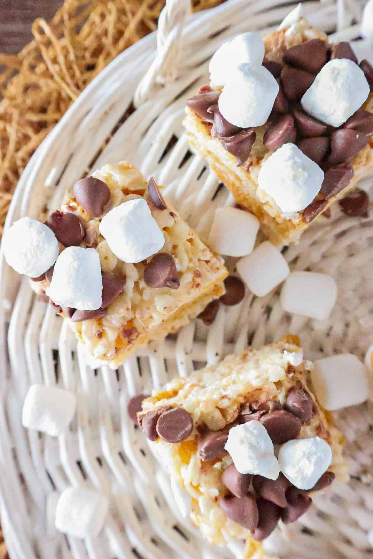 Three S'mores Rice Krispie treats topped with chocolate chips and mini marshmallows on a white basket.