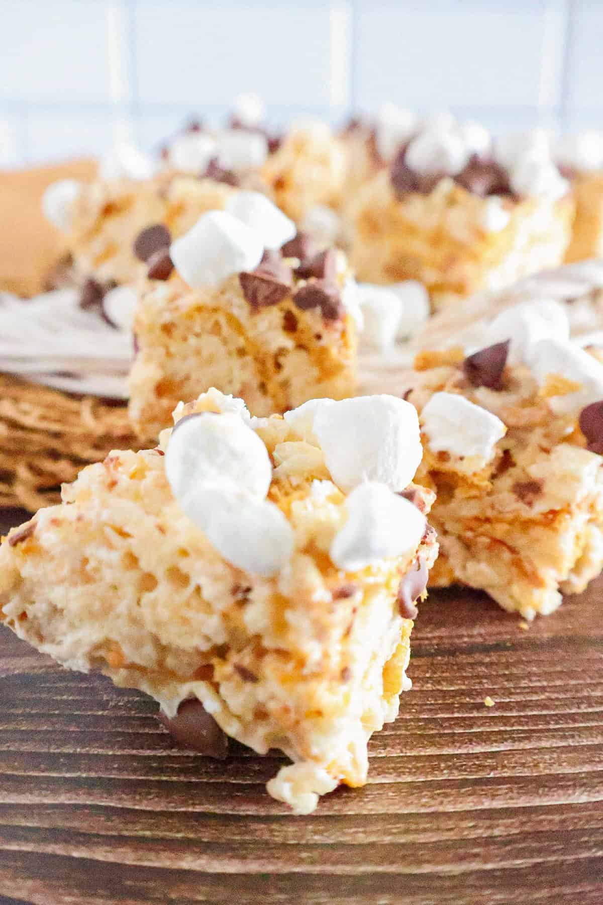 S'mores Rice Krispie treats topped with mini marshmallows and chocolate chips on a wooden table.