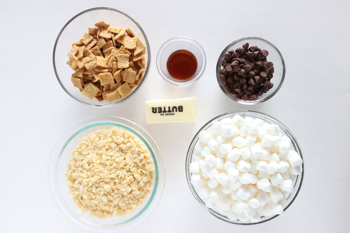Ingredients for S'mores Rice Krispie treats including Rice Krispies cereal, Golden Grahams, mini marshmallows, chocolate chips, butter, and vanilla.