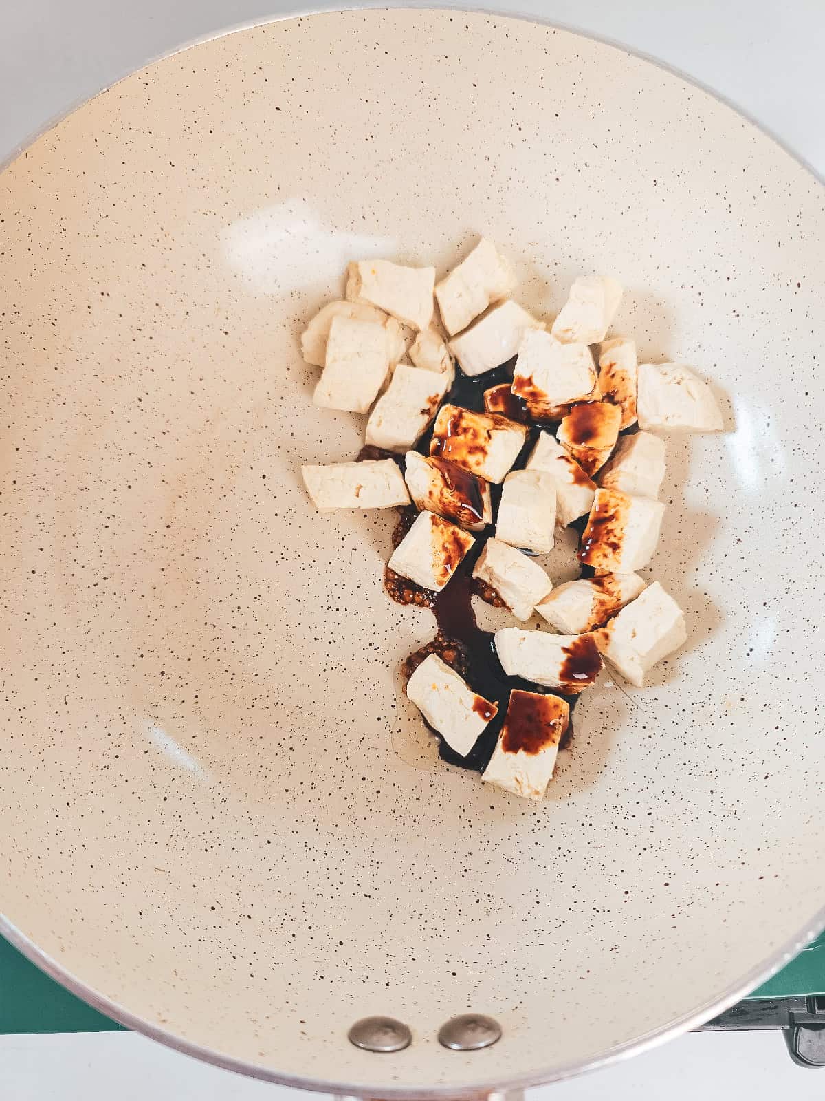Tofu cubes cooking in a skillet with soy sauce for vegan nasi goreng.