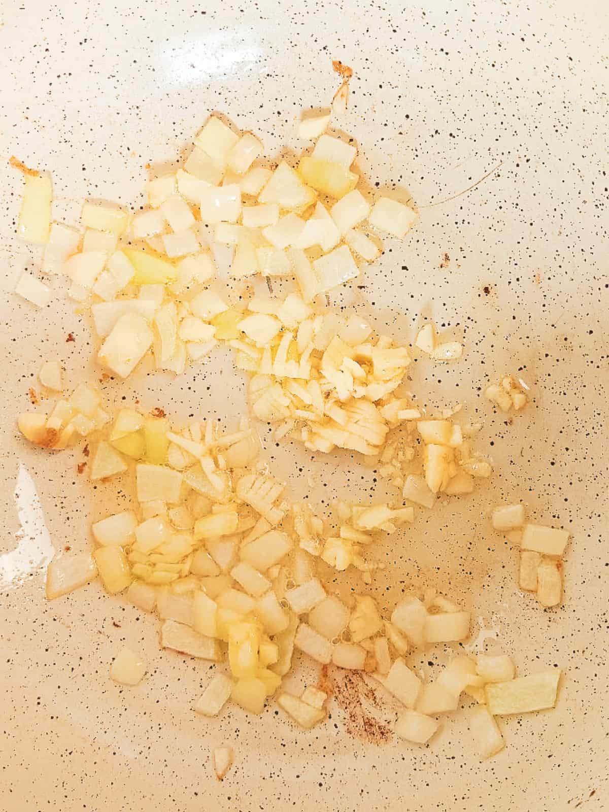 Chopped onion and garlic saut&eacute;ing in a skillet for vegan nasi goreng.