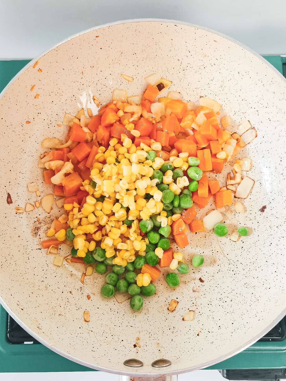 Carrots, corn, and peas cooking with onion and garlic in a skillet for vegan nasi goreng.