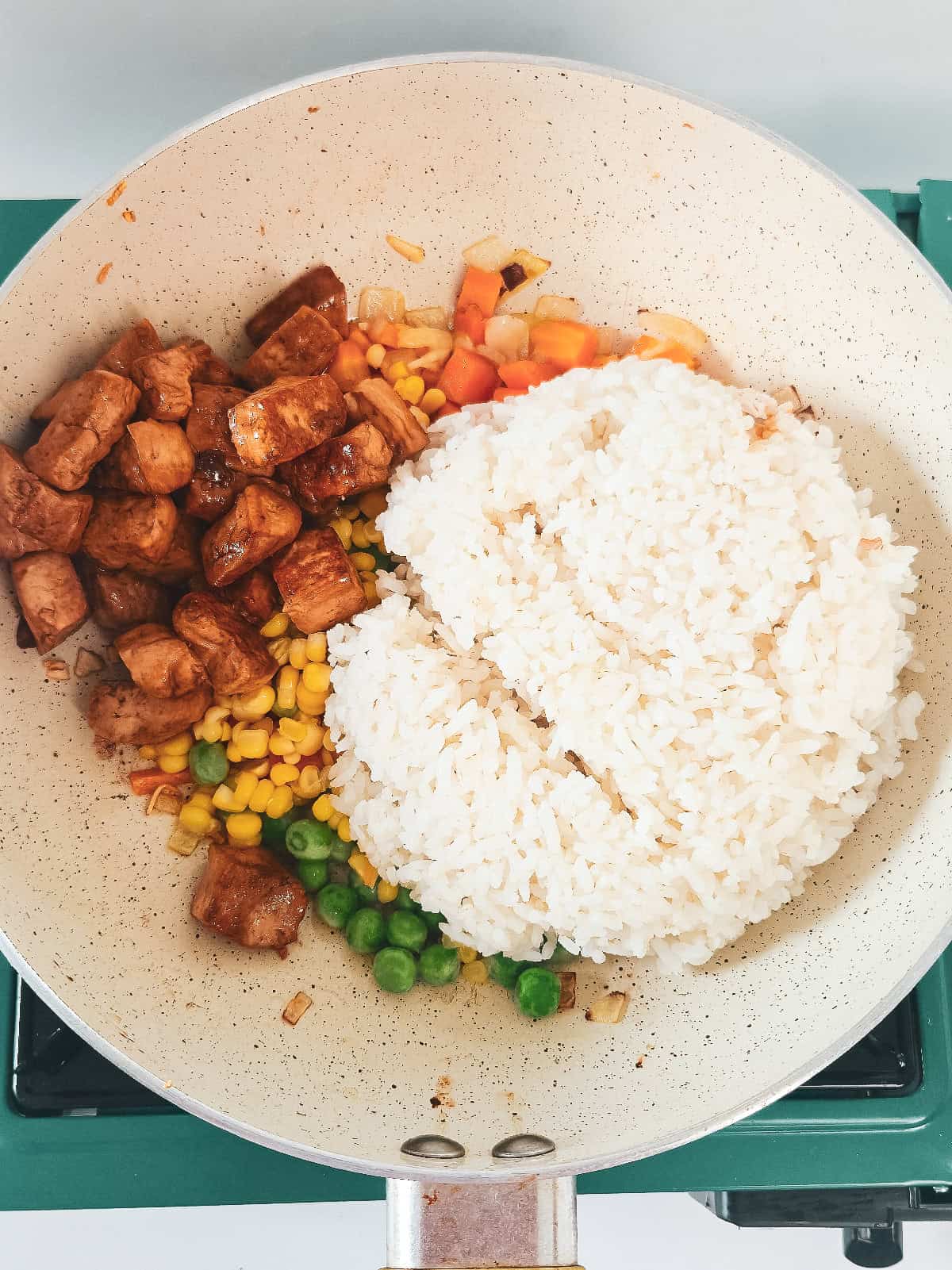 Cooked rice and browned tofu added to the vegetables in a skillet for vegan nasi goreng.