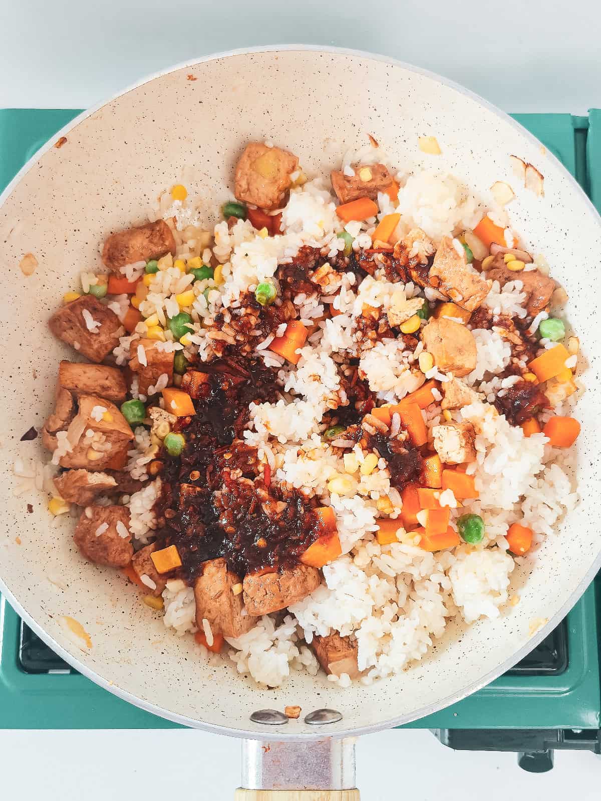 Sauce poured over rice, tofu, and vegetables before mixing for vegan nasi goreng.