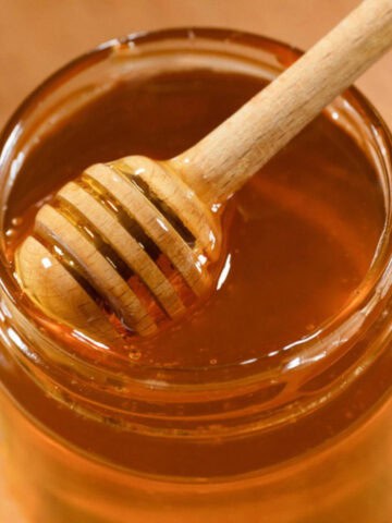 Honey dipper resting in a jar of honey on a wooden surface.
